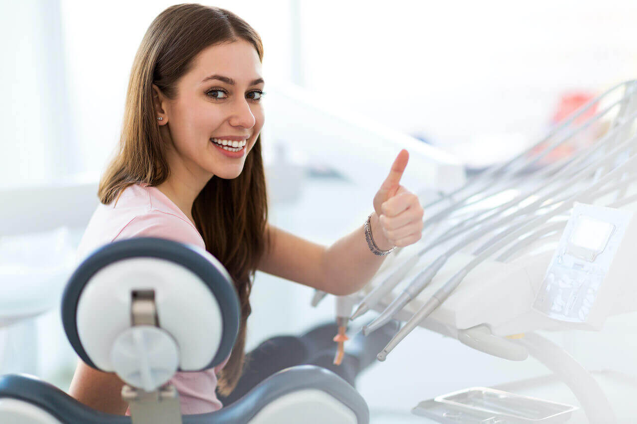 A young woman giving thumbs up at dental office. Keep your teeth healthy! Request An Appointment Langley Dental for your regular dental exam and dental cleaning.