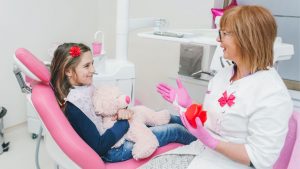 a child's first dental appointment - young girl holding a stuffed animal talking to her dentist
